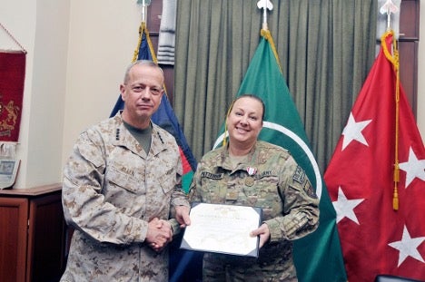 U.S. military personnel holding a certificate in front of service flags.