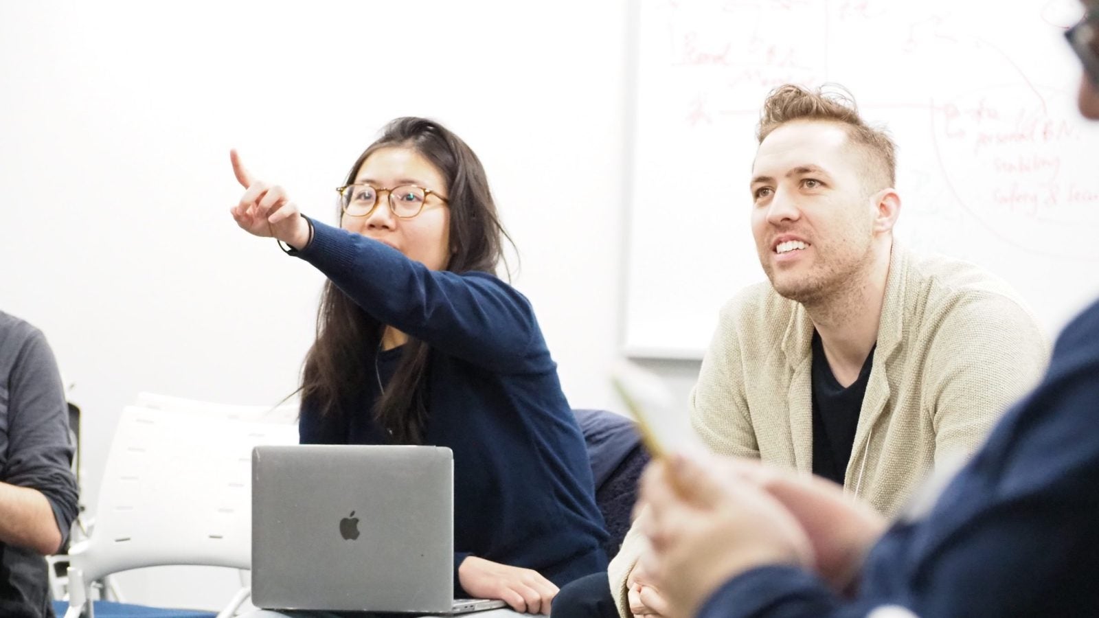 Two students sitting in a classroom, looking forward, one is pointing a finger.