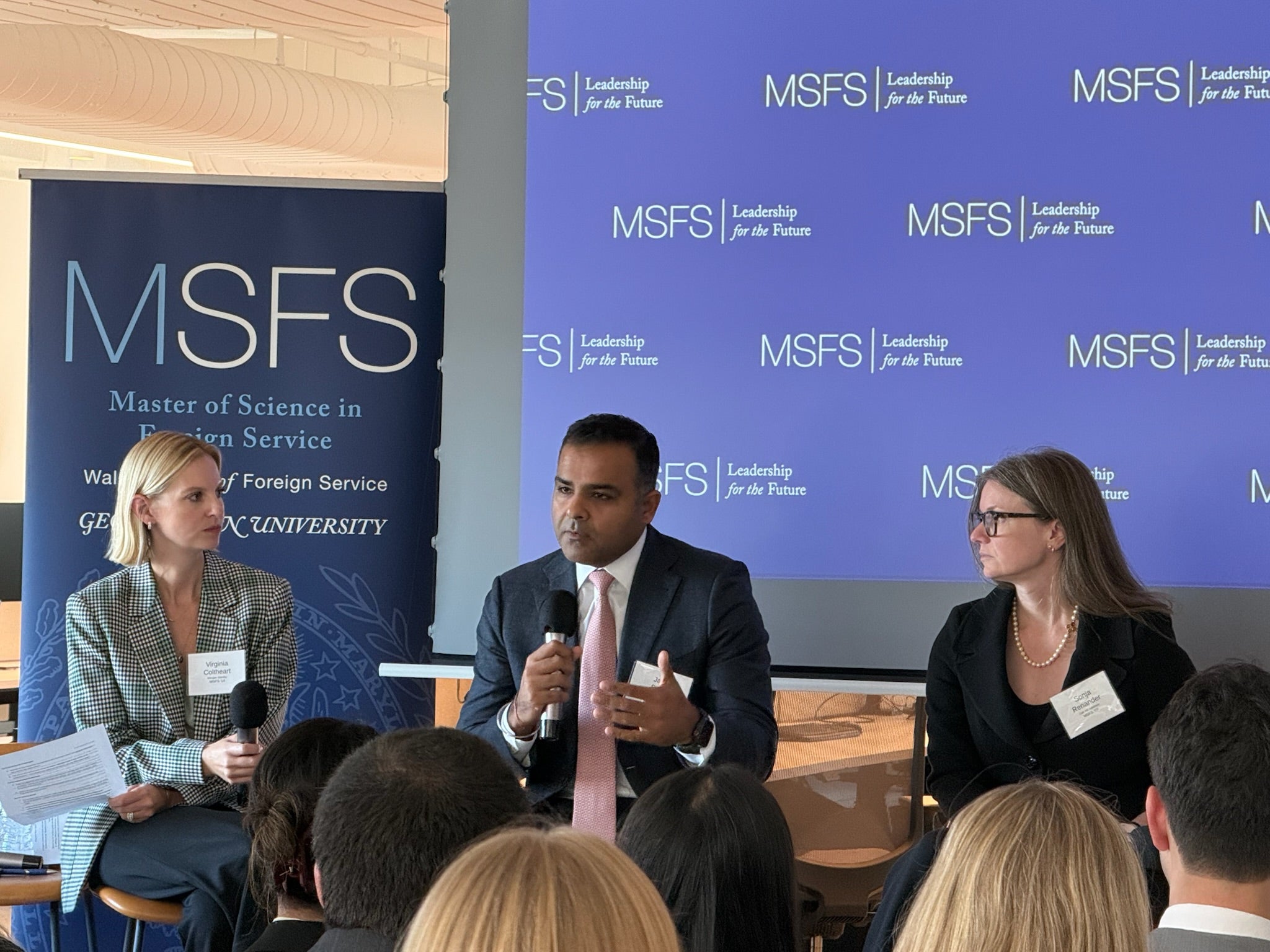 Three people engaging in a panel discussion in front of a seated audience. Behind them MSFS signs.