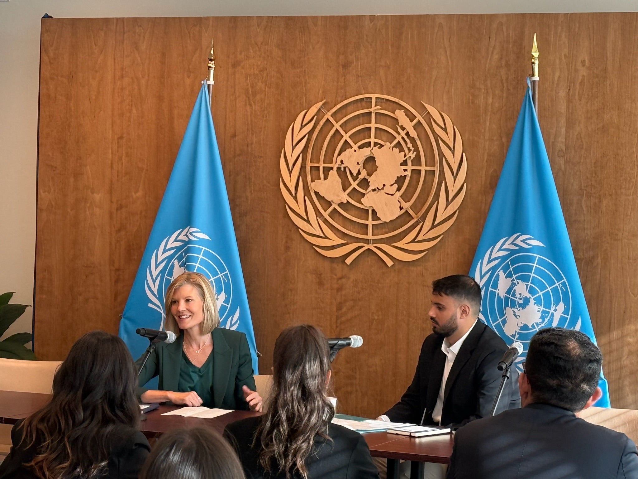 Two people engaging in conversation in front of an audience. Behind them the logo of the United Nations.