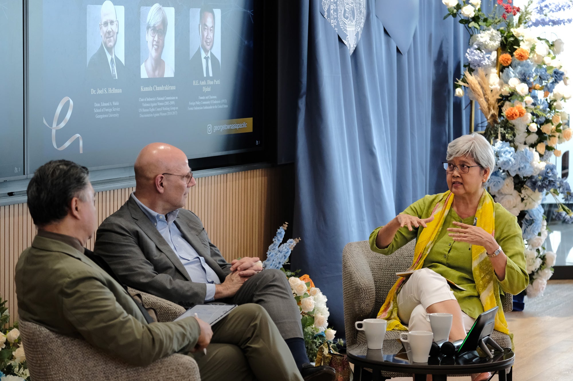Three people sitting in chairs having a conversation in front of an audience. 