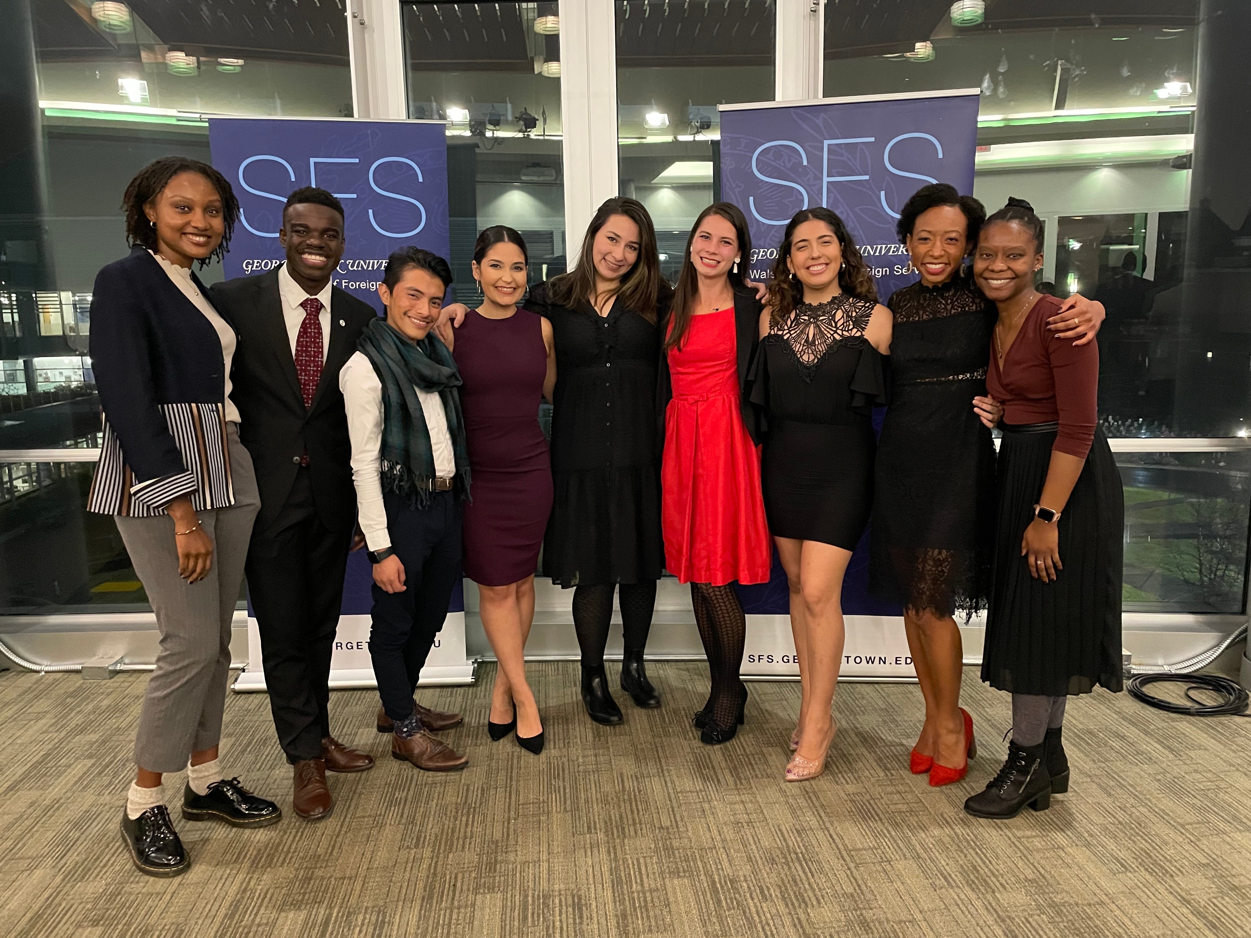 Group of eight individuals smiling at a Georgetown University School of Foreign Service event, standing in front of banners with the university's name.