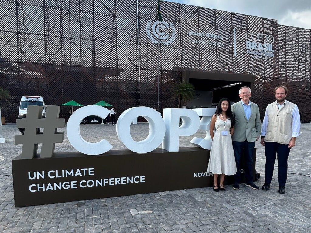 Three people standing next to the large COP30 "Un Climate Change Conference" sign