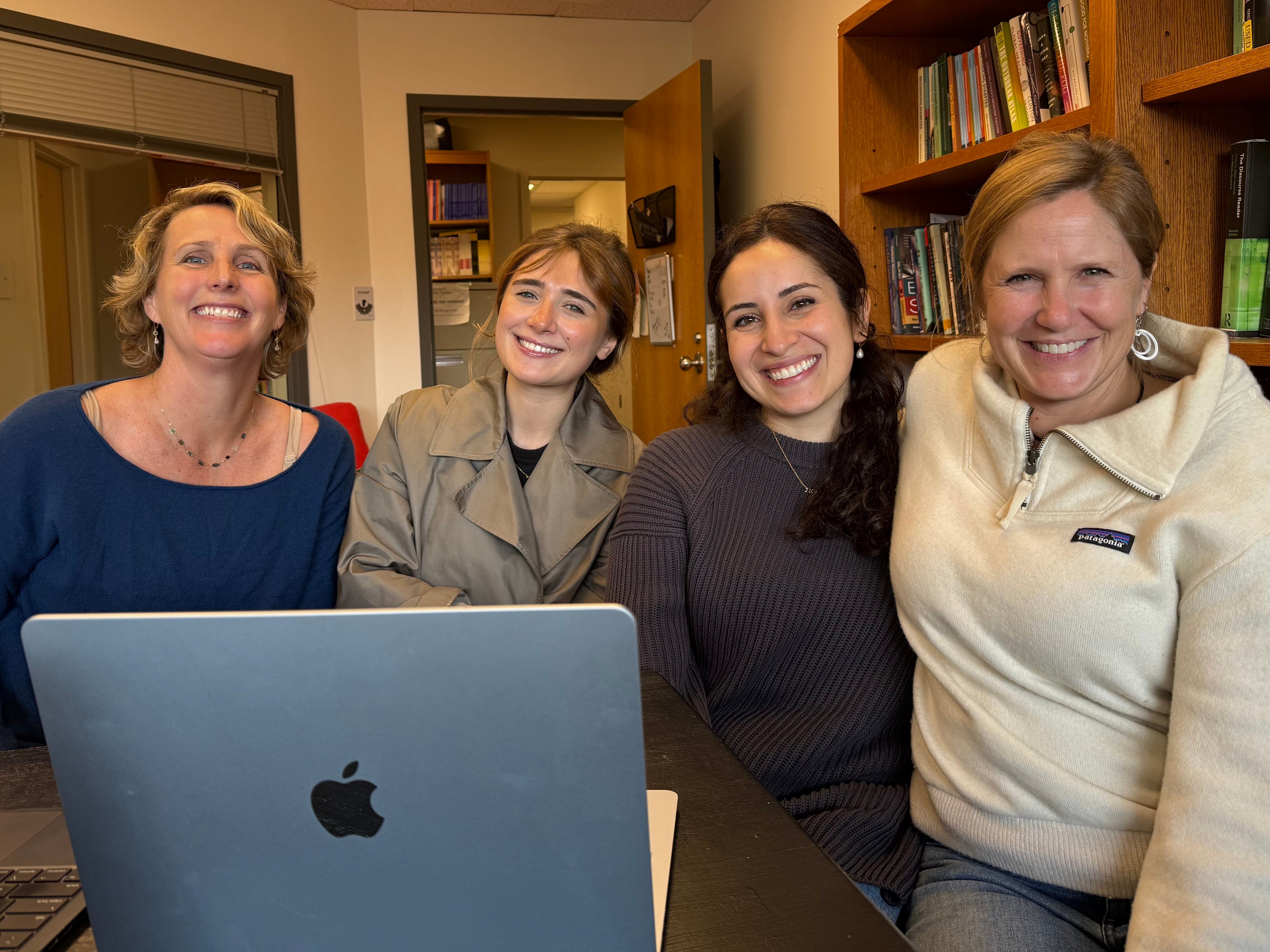 Four women sitting in an office with a laptop in front of them.