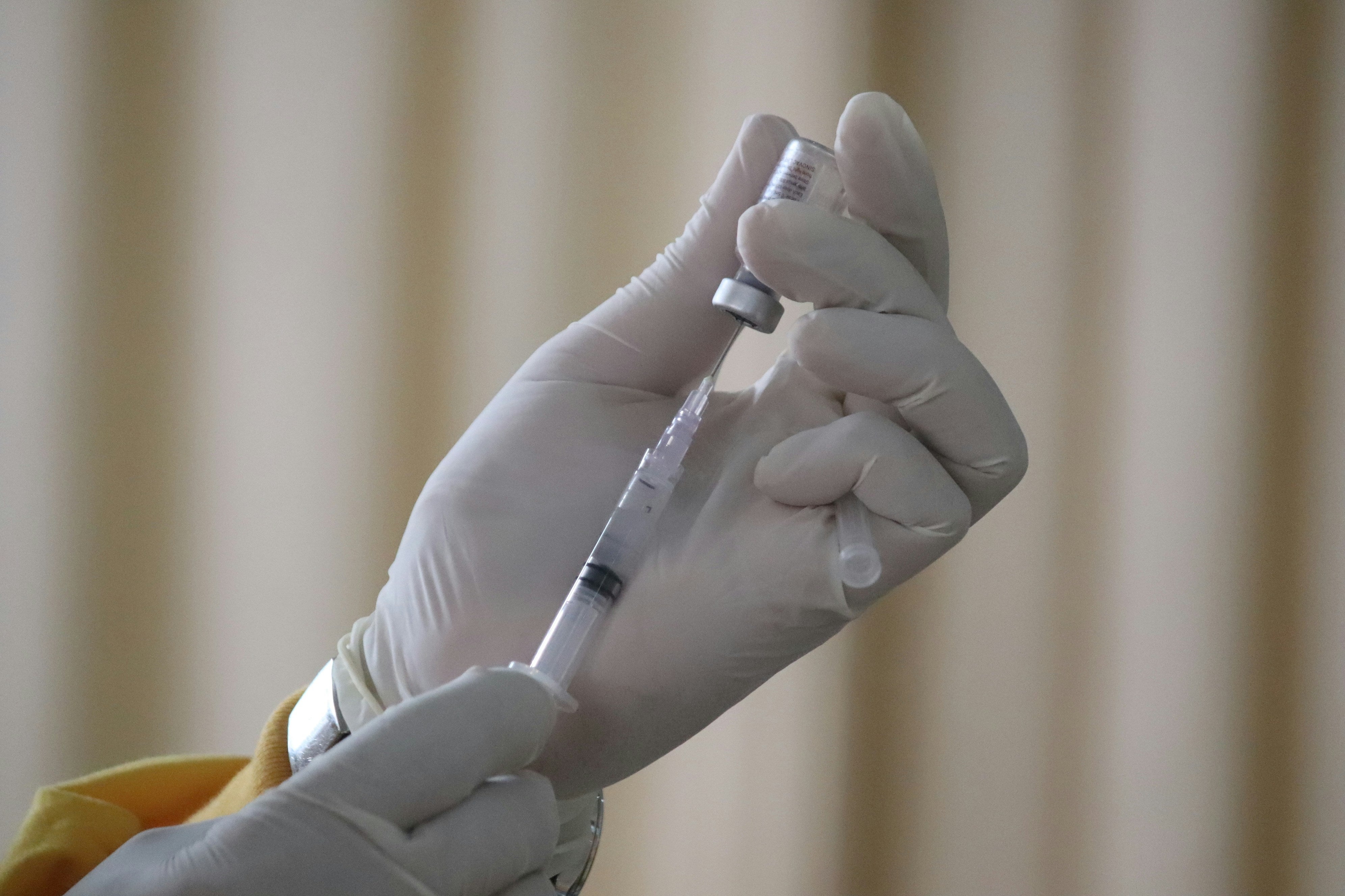 Gloved hands pull vaccine into a syringe from a vial.
