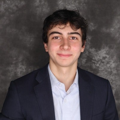 A young man with short brown hair wearing a blue shirt and black blazer.