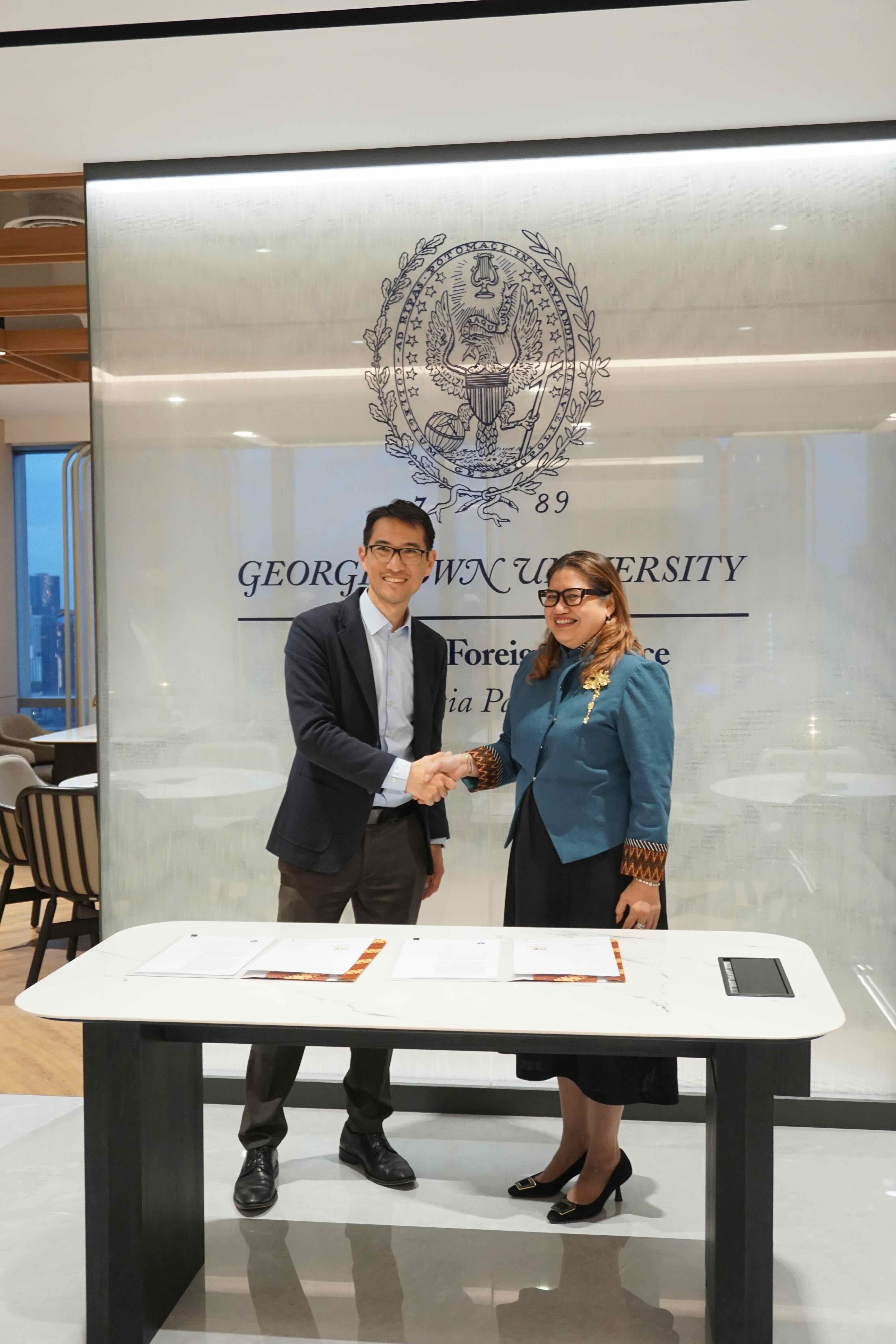 Two representatives from Bappeda DKI Jakarta and Georgetown SFS Asia Pacific share hands in front of a Georgetown backdrop