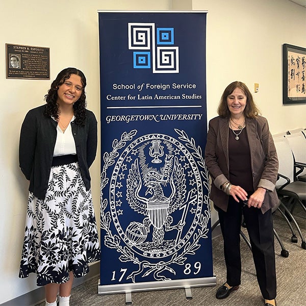 Kira and a professor standing on either side of a Georgetown poster.