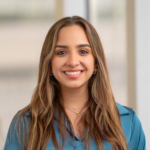 Antonella Termini, long brown hair with highlights, warm smile, teal blouse, layered necklaces, hoop earrings