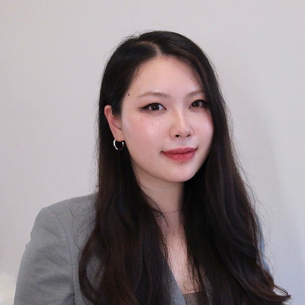 Bohan Chen, long dark hair, light skin, subtle smile, gray blazer, hoop earrings, neutral background