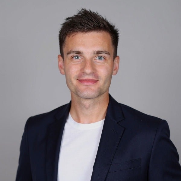 Brendan Sanders, dark brown styled hair, blue eyes, light stubble, warm smile, white shirt, navy blazer