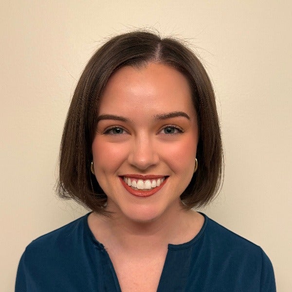 Brenna Recny, dark brown bob-length hair, warm smile, teal blue top, beige background