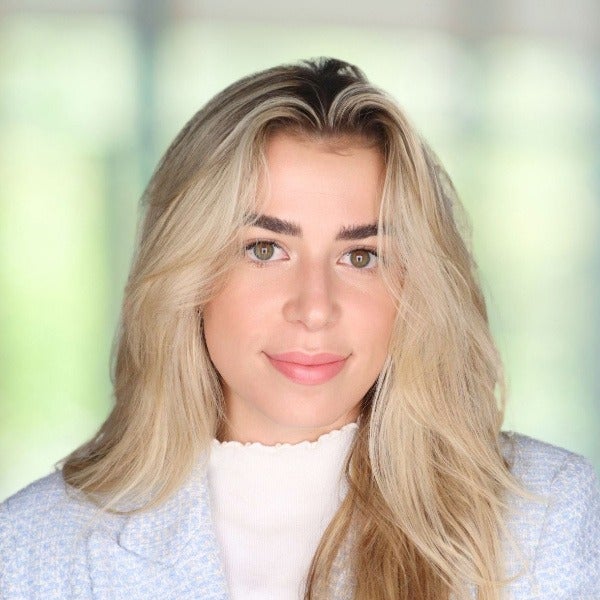 Bri Harnack, blonde hair with darker roots, green eyes, soft smile, white top, light blue sweater