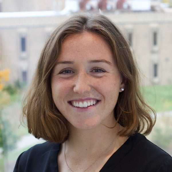 Bronwyn Shields, shoulder-length brown hair with highlights, bright smile, black top, small earrings, outdoor background