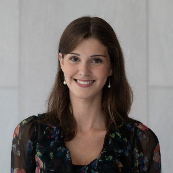 Caroline Smutny, brown shoulder-length hair, warm smile, floral sheer blouse with black underlay, pearl earrings