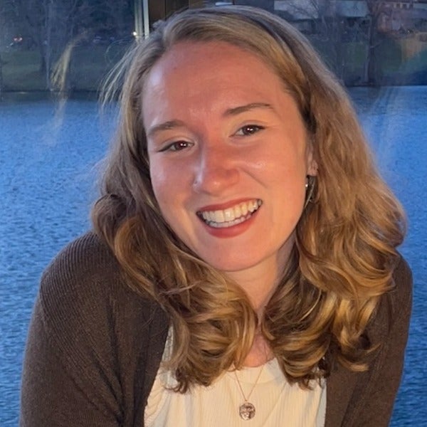 Ellie Murphy, shoulder-length wavy blonde hair, bright smile, brown cardigan over light top, blue water background