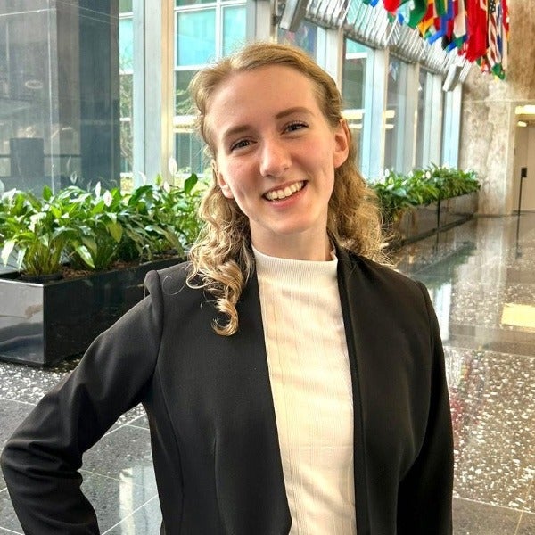 Emily Houtz, blonde wavy hair, bright smile, cream turtleneck, black blazer, indoor atrium setting