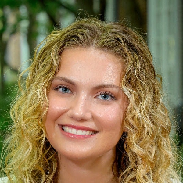 Grace Mahony, blonde wavy shoulder-length hair, blue eyes, warm smile, natural makeup, black top