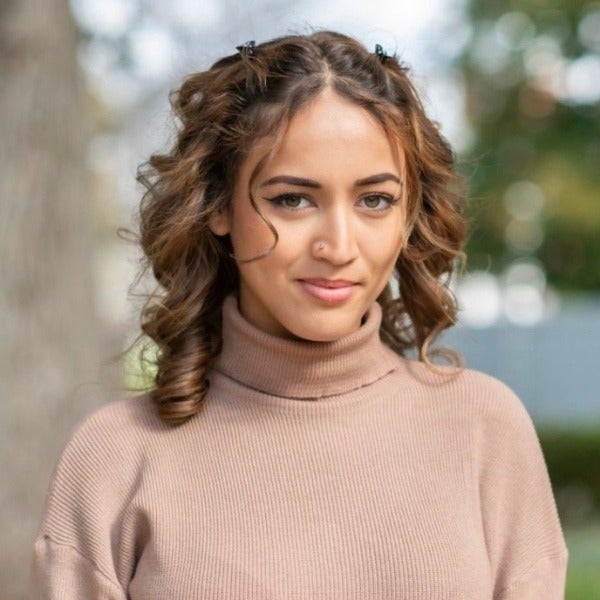Ibtisam Alafghani, brown curly hair in braids, warm smile, beige turtleneck sweater, outdoor setting