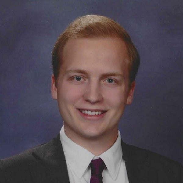Jack Schallich, short reddish-brown hair, fair skin, smiling, dark suit with white shirt and burgundy tie