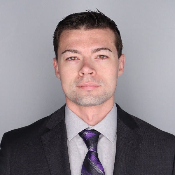 Jacob Knack, short dark hair, light stubble, black suit, gray shirt, purple striped tie, neutral expression