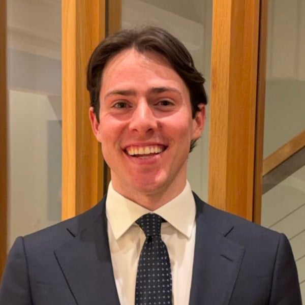 Jake Laming Free, dark brown hair swept to side, bright smile, navy suit, polka dot tie, wooden frame background