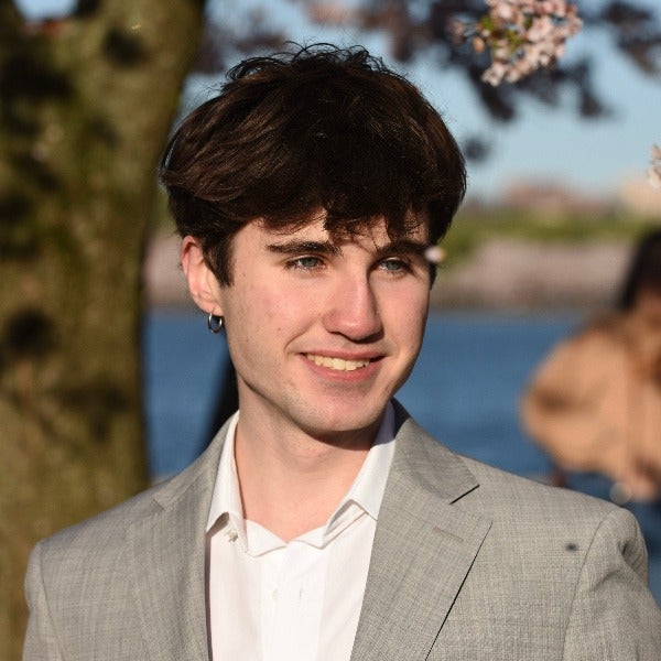 Jean Luc Euzen, dark wavy hair, earring, light blazer over white collared shirt, smiling outdoors