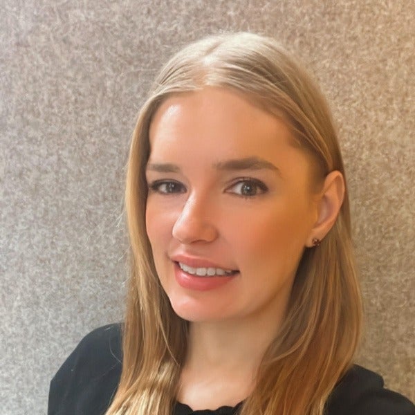 Kate Hartnett, blonde shoulder-length hair, warm smile, black top, textured gray background
