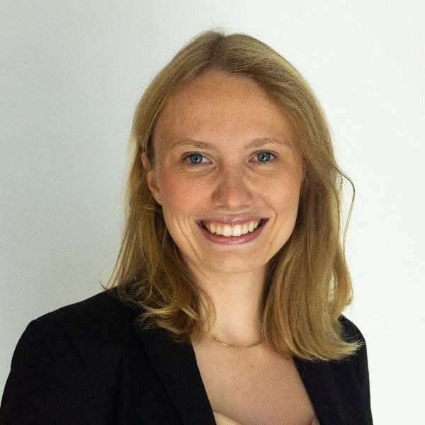 Kathryn Putz, blonde shoulder-length hair, warm smile, black blazer, delicate necklace, light background