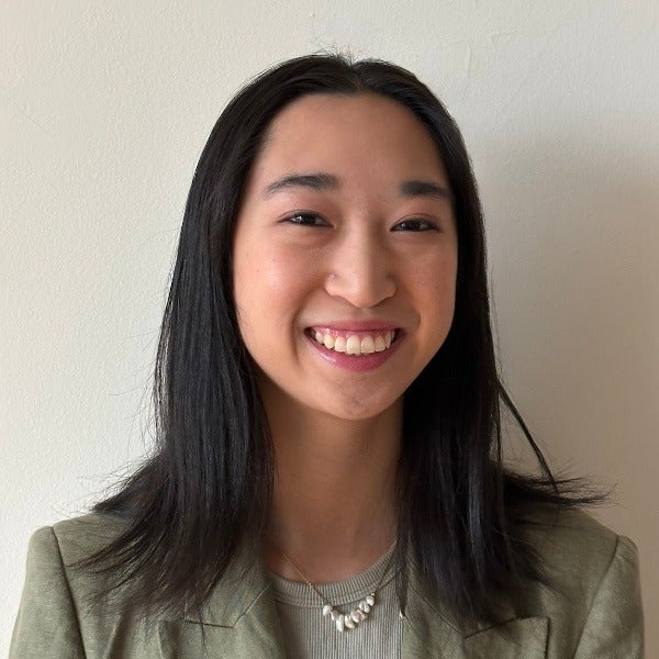 Maeve Wong, long straight black hair, warm smile, olive blazer, pearl necklace, light background