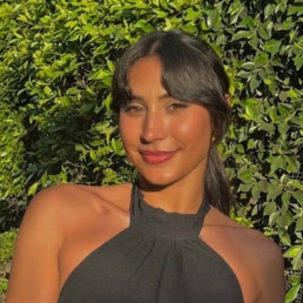 Maria Roth, long dark hair, warm smile, olive skin tone, black halter top, green foliage background