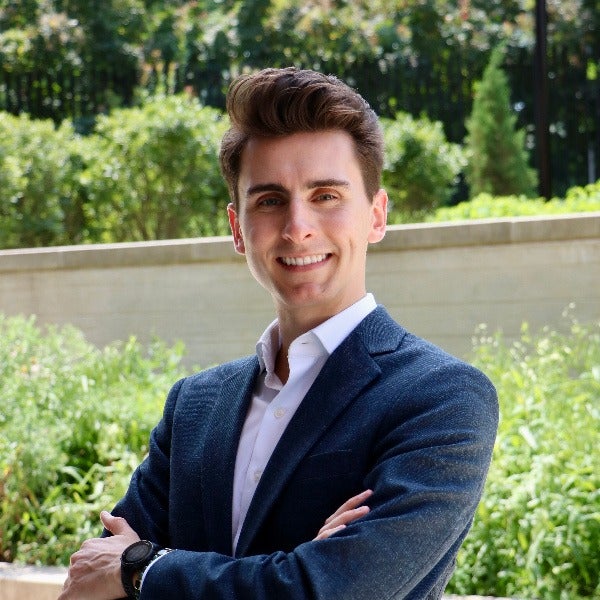 Matthew Boyle, brown styled hair, warm smile, white shirt, navy textured blazer, arms crossed, outdoor garden setting