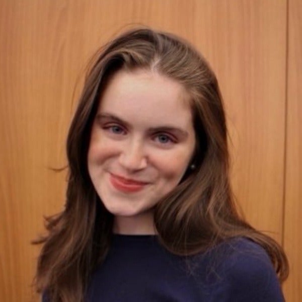 Mercedes Sapuppo, shoulder-length brown hair, warm smile, navy blue top, light skin tone, wood background
