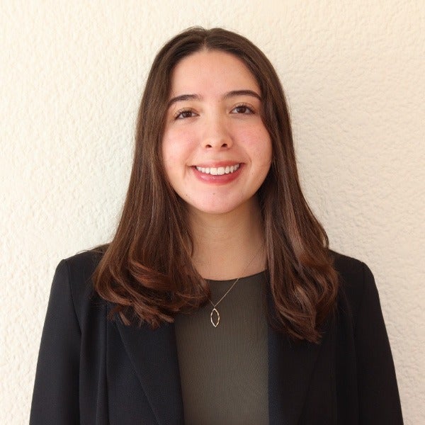 Montserrat Zeron, long brown hair, warm smile, black blazer over olive top, delicate necklace