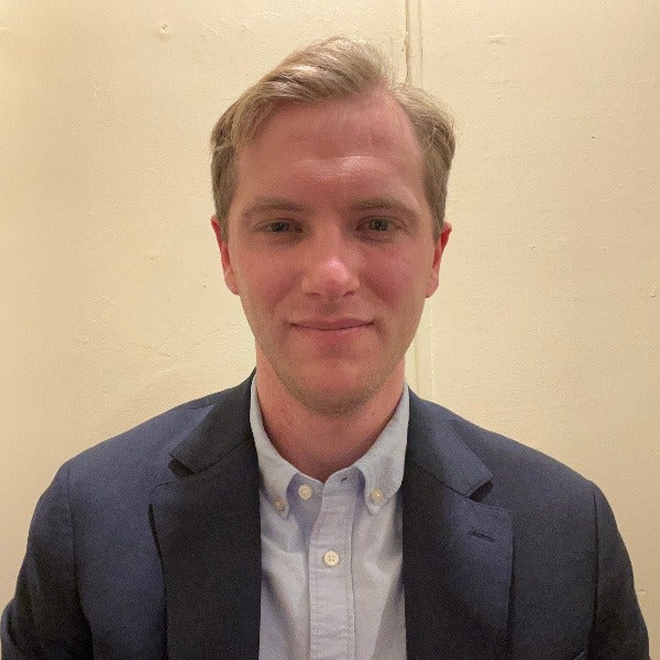 Nicholas Pomper, light brown hair swept aside, fair complexion, slight smile, navy blazer over light blue button-down shirt