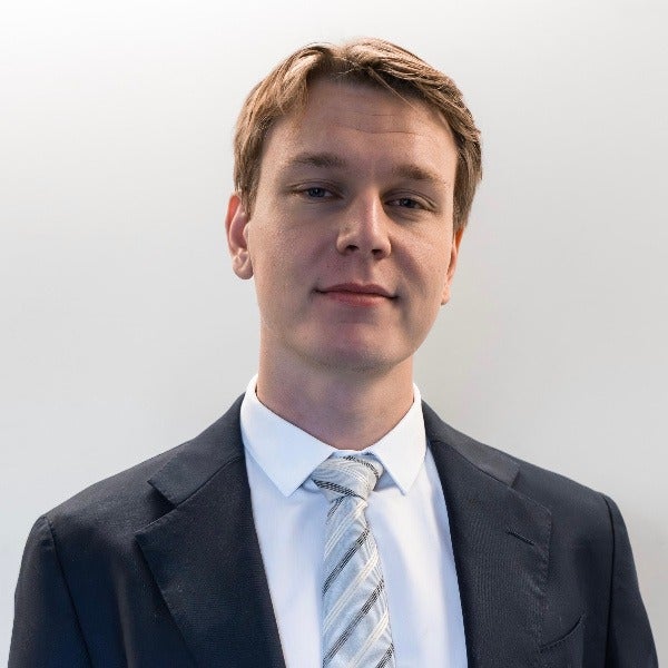 Oskar Jansson, light brown hair swept to side, light skin, slight smile, dark suit, striped tie, white background