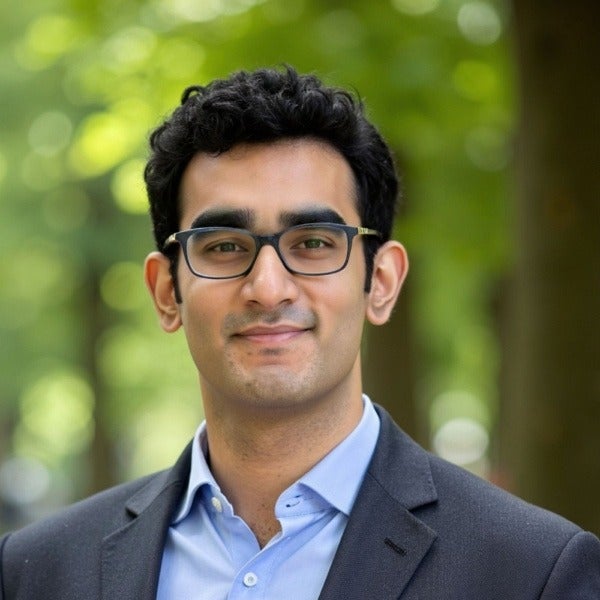 Sahil Sonalkar, dark curly hair, black-framed glasses, light blue shirt, dark blazer, gentle smile