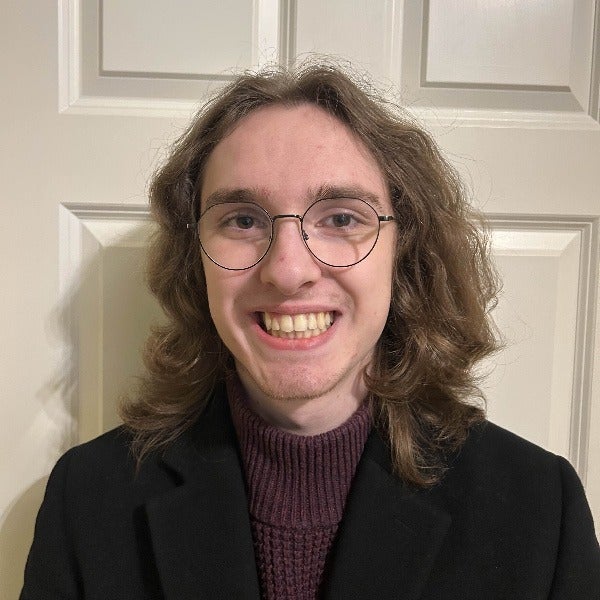 Samantha Kelley, straight brown hair with lighter ends, glasses, warm smile, beige blazer over white top