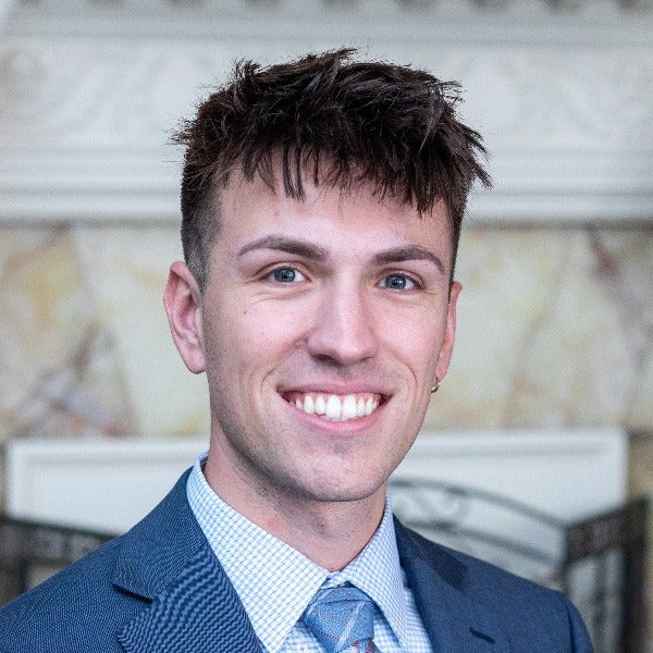 Sean Bierman, dark textured hair, bright smile, navy suit, light checkered shirt, blue tie