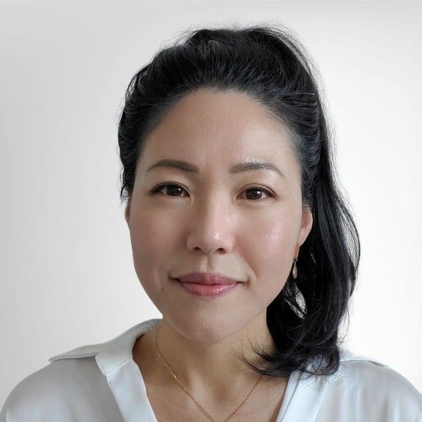 Shilla Kang, black hair pulled back, warm smile, white blouse with sheer sleeves, light background