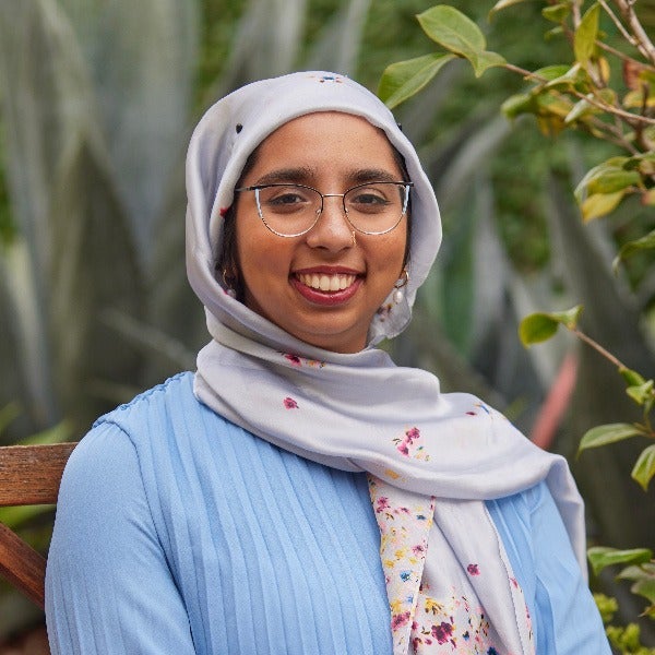 Warisha Siddiqui, floral hijab, glasses, warm smile, light blue top, outdoor garden setting