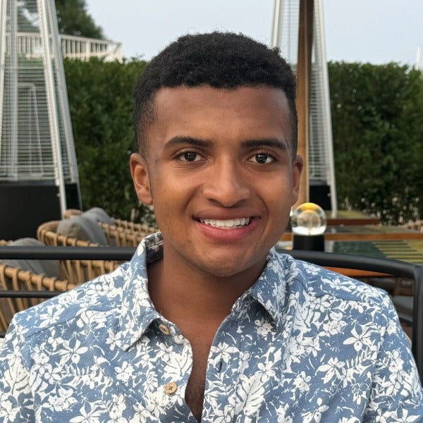 Wyatt Weekes, short dark curly hair, warm brown skin, bright smile, blue floral shirt, outdoor setting