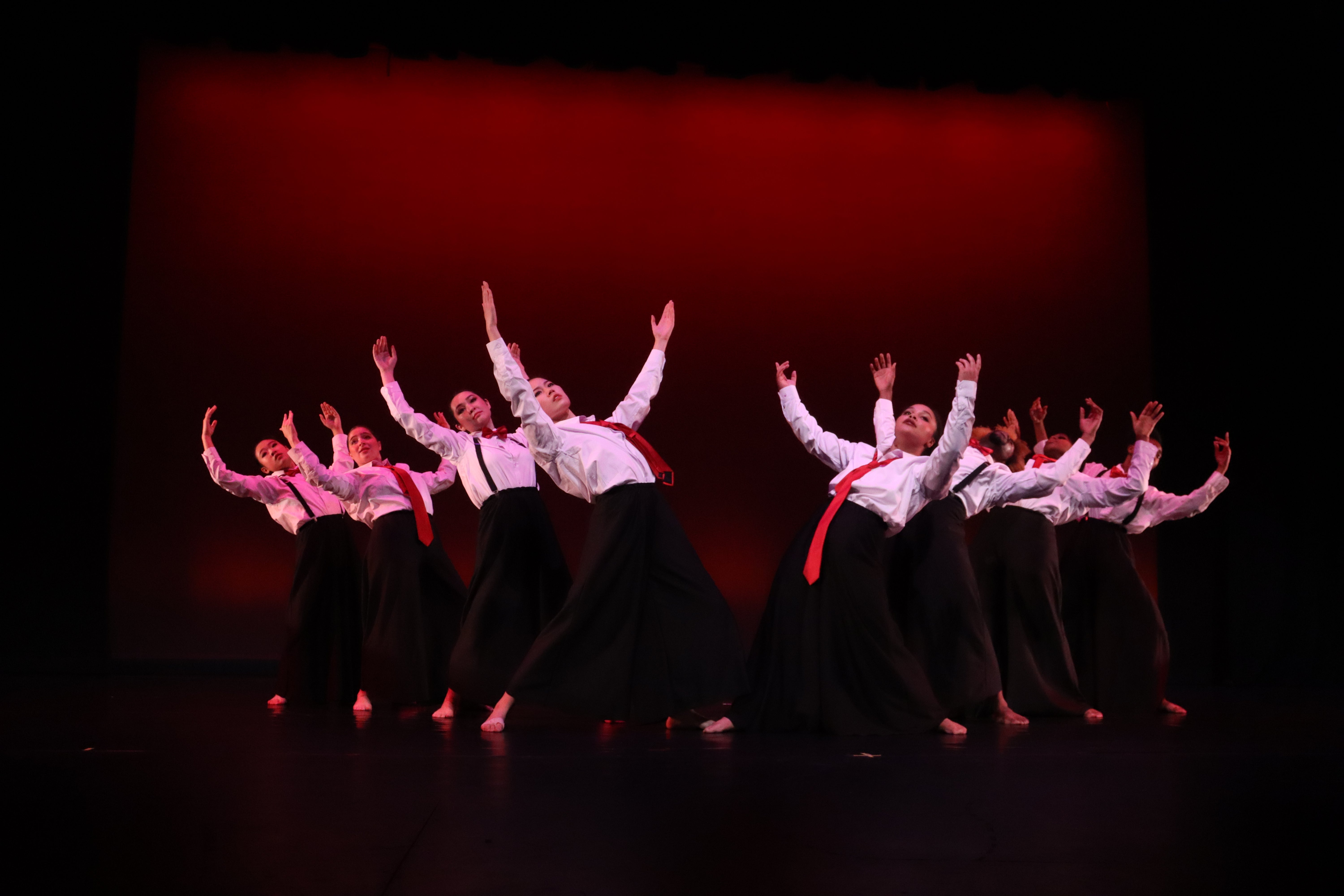 A group of dancers wearing white collared shirts and ties throw their hands up as part of their performance.