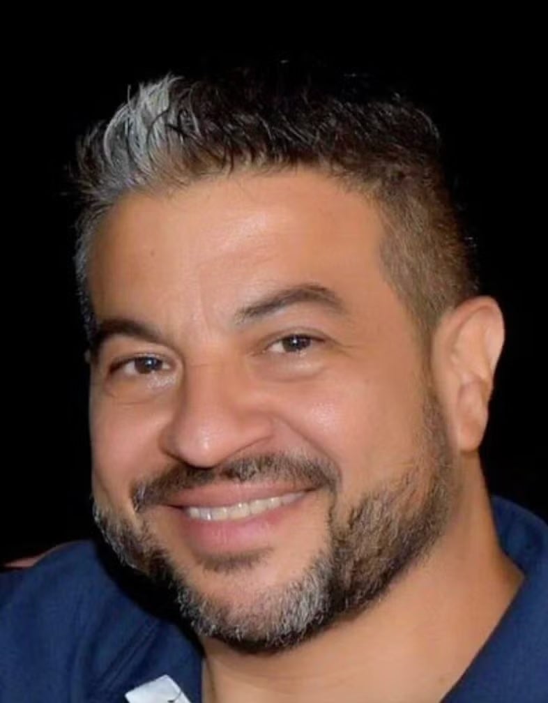 A headshot of an individual with short black hair and beard.