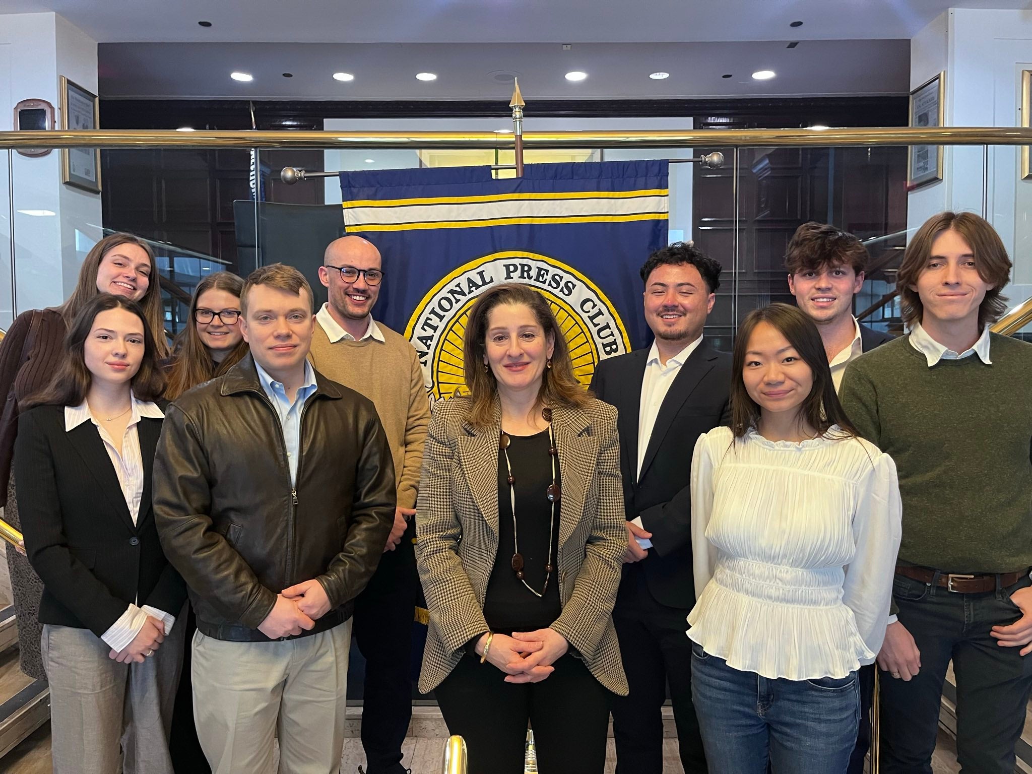 Ten people in two lines smile in front of a banner that says "National Press Club."
