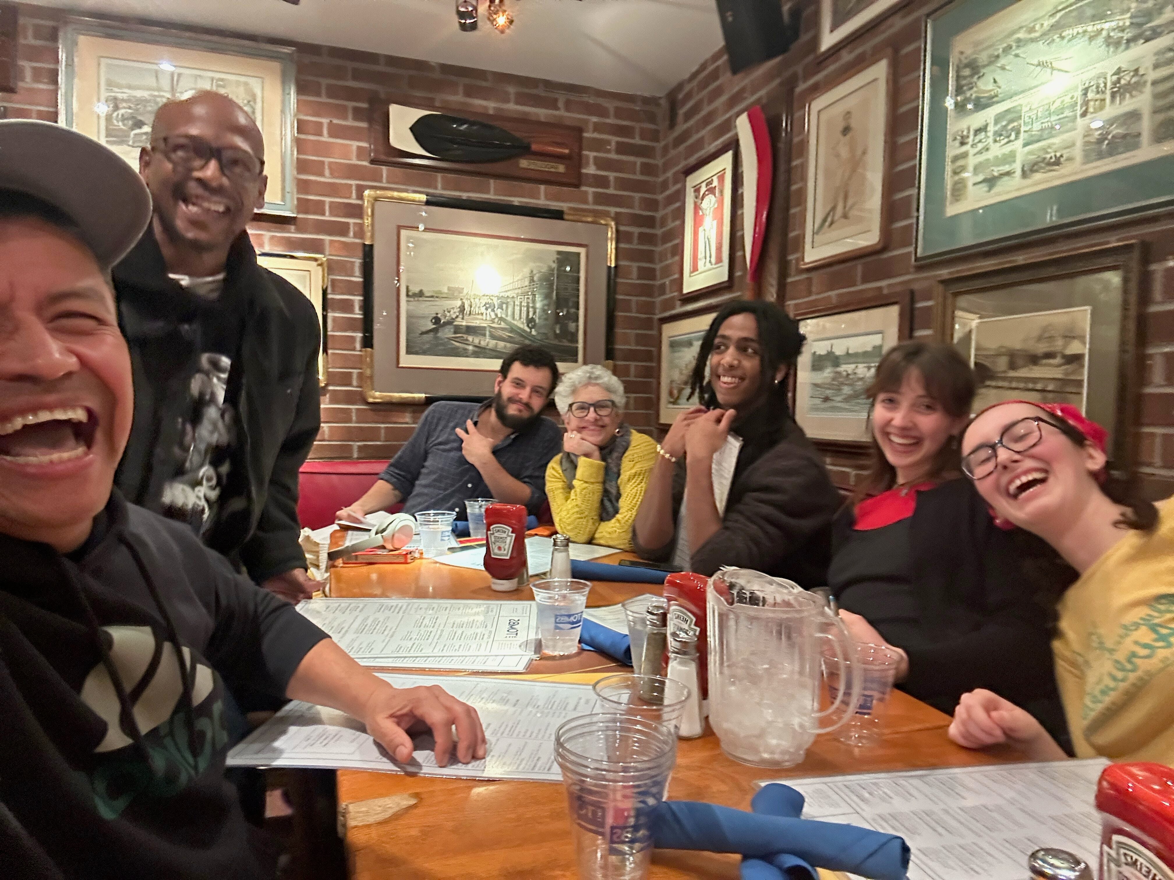 A group of people laugh together as they take a selfie at a dinner table.
