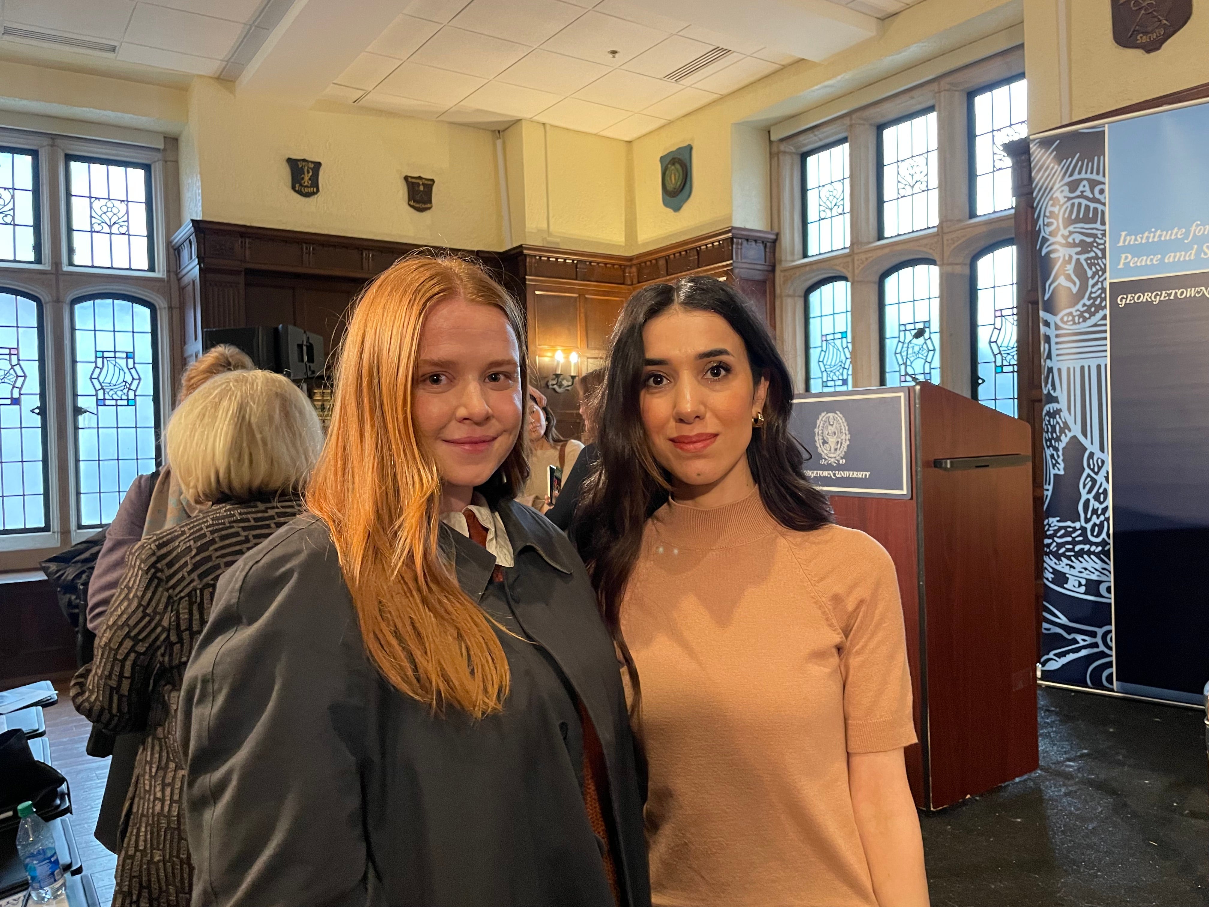 Two individuals wearing business attire stand in a conference room setting.