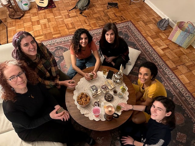 Six women seated at a low table with dishes covering it.