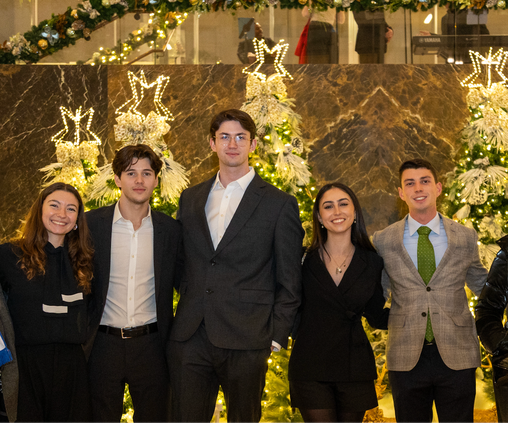 Two young women and three young men pose in front of a Christmas tree display.