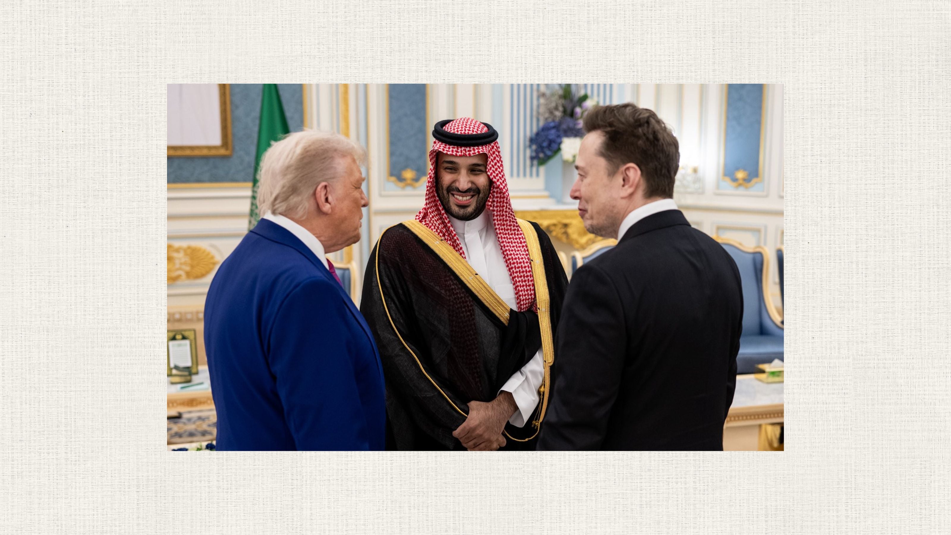 A group of three individuals are engaged in conversation in an opulent room. Two of them stand with their backs partially to the viewer, while the third faces them, smiling. A flag and luxurious furnishings are visible in the background.